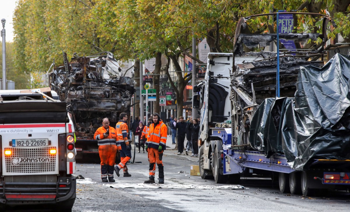 Des ouvriers enlèvent les débris de la route alors que les carcasses des bus brûlés attendent d'être enlevées de la rue O'Connell à Dublin, le 24 novembre 2023, après une nuit de protestations. (Photo Paul Faith AFP)