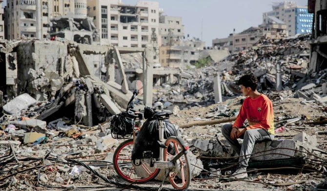 Un jeune palestinien est assis à coté de son vélo au milieu des décombres de bâtiments détruits à Gaza (AFP)