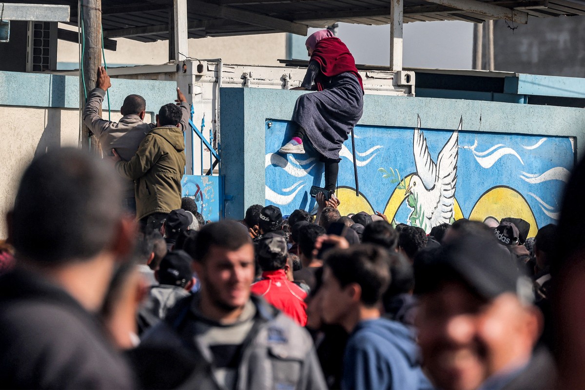 Une femme palestinienne escalade un mur pour entrer dans un entrepôt de l'Office de secours et de travaux des Nations Unies pour les réfugiés de Palestine (UNRWA) après avoir fait la queue pour recevoir des rations de farine, à Rafah, dans le sud de la bande de Gaza, le 12 décembre 2023, alors que les combats se poursuivent entre Israël et le Hamas. (Photo par Mohammed Abed AFP)