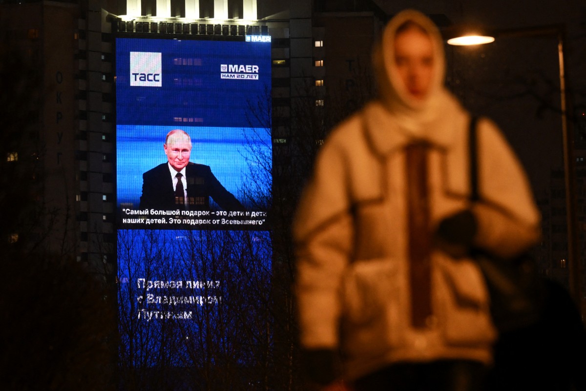 Un écran géant diffusant la conférence de presse de fin d'année du président russe Vladimir Poutine est visible sur la façade d'un immeuble résidentiel alors qu'une femme marche dans une rue de Moscou, le 14 décembre 2023. (Photo Natalia Kolesnikova AFP)