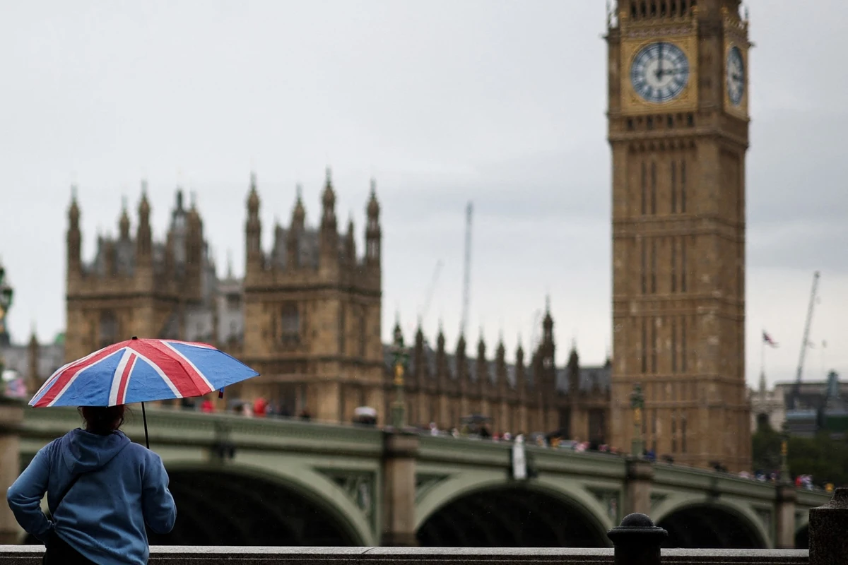 Abrité sous un parapluie représentant l'Union Jack, un piéton regarde la tour Elizabeth, communément appelée Big Ben, depuis la rive sud de la Tamise, dans le centre de Londres, le 31 juillet 2023, par une journée d'été maussade et pluvieuse. (Photo Henry Nicholls AFP)