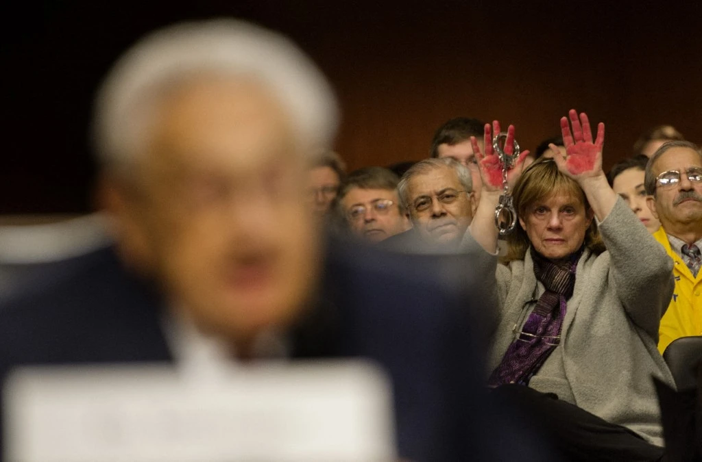 Une manifestante CodePink brandit des mains "ensanglantées" et des menottes qualifiant l'ancien secrétaire d'État américain Henry Kissinger (à gauche) de criminel de guerre alors qu'il s'exprime lors d'une audition de la commission des forces armées du Sénat américain sur les "défis mondiaux et la stratégie de sécurité nationale des États-Unis" au Capitole à Washington, DC, le 29 janvier 2015. (Photo Jim Watson AFP)