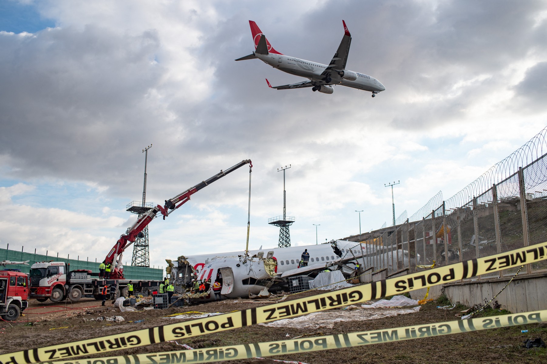 Un avion de Turkish Airlines se prépare à l'atterrissage alors que des ouvriers enlèvent l'épave du Boeing 737 de Pegasus Airlines à Istanbul, le 9 février 2020, quatre jours après que l'avion ait dérapé sur la piste d'atterrissage de l'aéroport Sabiha Gokcen. La Turquie va enquêter sur deux pilotes pour négligence éventuelle après que leur avion a dérapé sur la piste d'atterrissage d'Istanbul, tuant trois passagers, ont rapporté les médias d'État le 7 février. (Photo Yasin Akgul AFP)