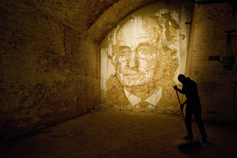 Un homme balaie le sol devant le portrait ciselé de Vhils intitulé "Bernie Made Off", lors de l'exposition "Hell's Half Acre" à l'Old Vic Tunnels dans le sud de Londres, le 11 octobre 2010. (Photo Leon Neal AFP)