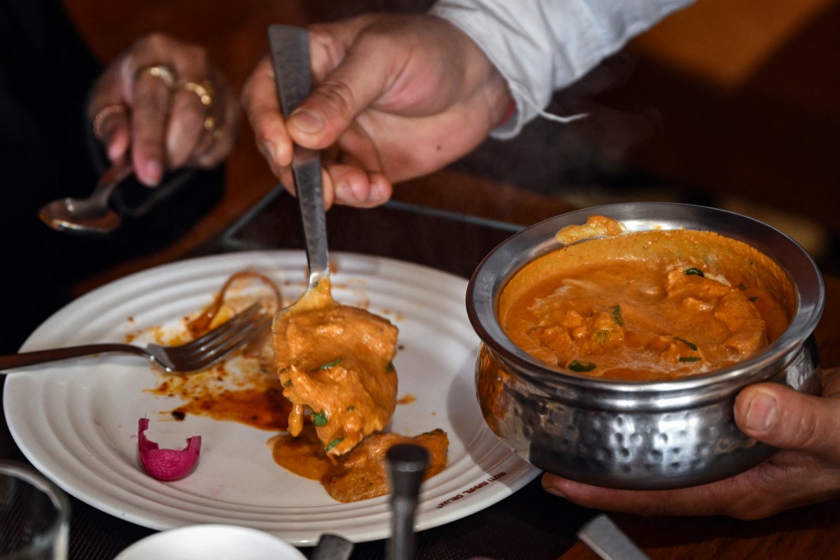 Sur cette photo prise le 29 janvier 2024, un serveur sert du poulet au beurre à des clients du restaurant Moti Mahal à New Delhi. Le poulet au beurre, l'un des plats les plus appréciés en Inde, est au cœur d'une tempête culinaire, deux chaînes de restaurants concurrentes affirmant être les inventeurs de cette préparation savoureuse. (Photo Arun Sankar AFP)