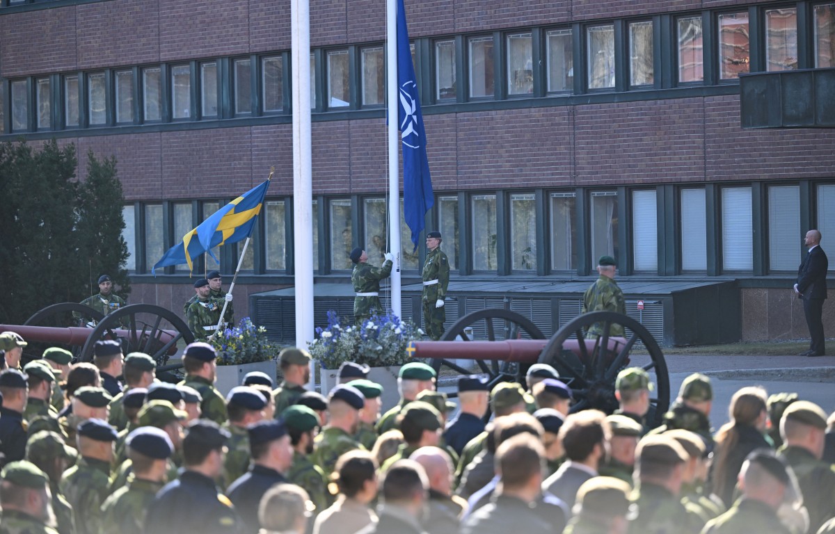 Des soldats suédois regardent le drapeau de l'OTAN (à droite) hissé devant le quartier général des forces armées suédoises à Stockholm, le 11 mars 2024, pour marquer l'entrée de la Suède dans l'alliance. La Suède devient le 32e membre de l'alliance militaire. (Photo Jonathan Nackstrand AFP)