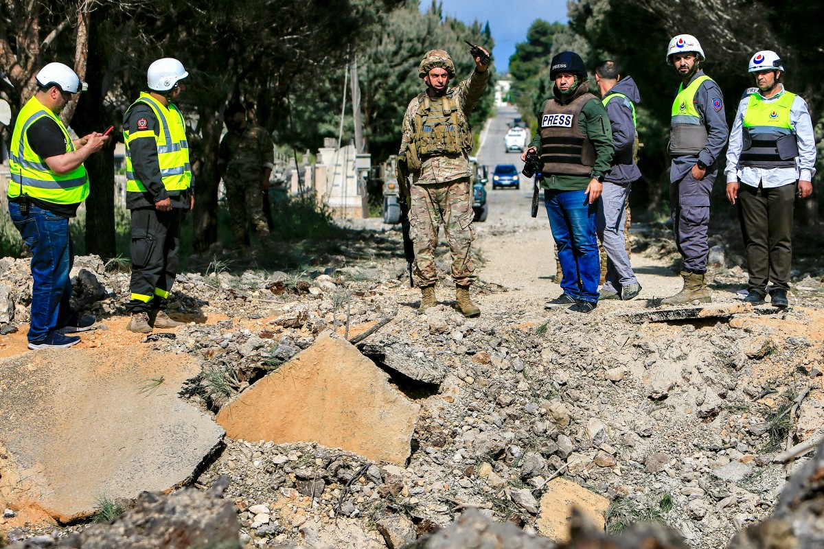 Un soldat de l'armée libanaise et des secouristes de la défense civile devant un cratère d'impact à la suite d'une frappe aérienne israélienne qui a touché une route dans le village d'Alma al-Shaab, au sud du Liban, le 15 avril 2024, dans un contexte de tensions transfrontalières continues. (Photo par AFP)