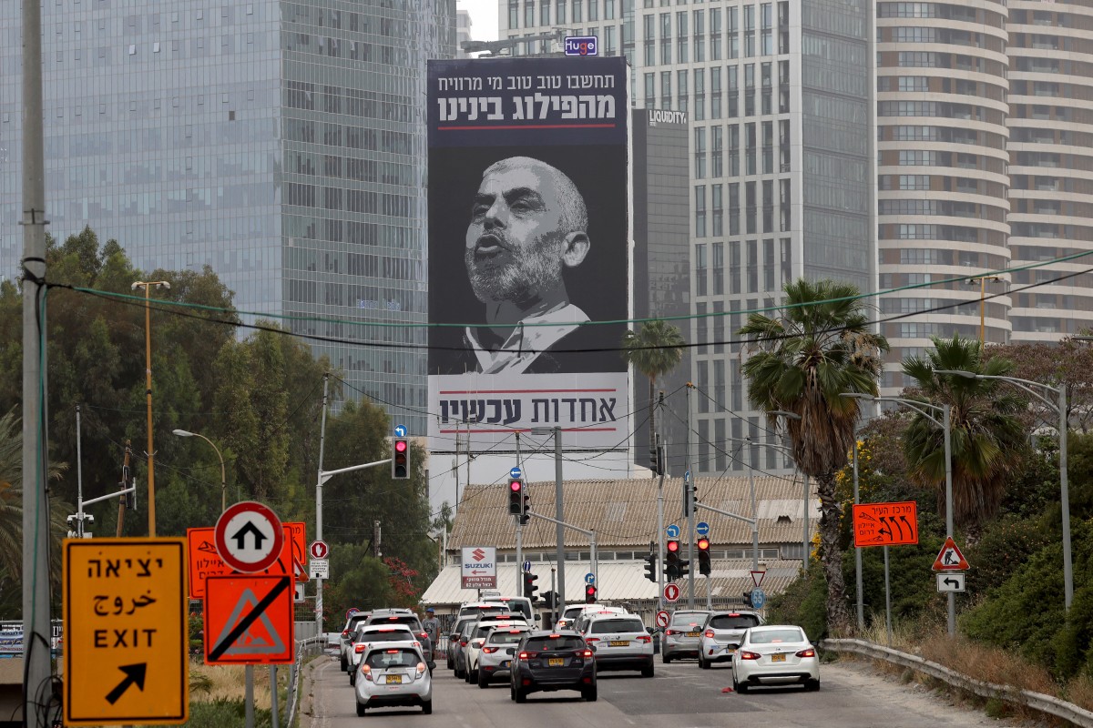 Des voitures passent devant un panneau d'affichage portant une inscription en hébreu "Pensez bien à qui profite notre division - l'unité maintenant", avec un portrait du chef de l'aile politique du mouvement palestinien Hamas dans la bande de Gaza Yahya Sinwar, à Tel Aviv le 26 avril 2024. (Photo par Jack Guez AFP)