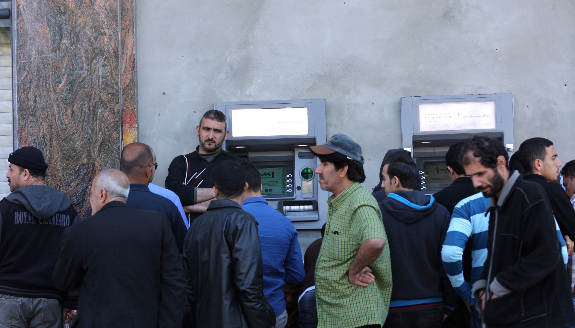 Des employés palestiniens font la queue devant un distributeur de billets à l'extérieur de la Banque de Palestine alors qu'ils attendent de retirer leur salaire, dans la ville de Gaza, le 9 avril 2018. (Photo de Mahmud Hams / AFP)