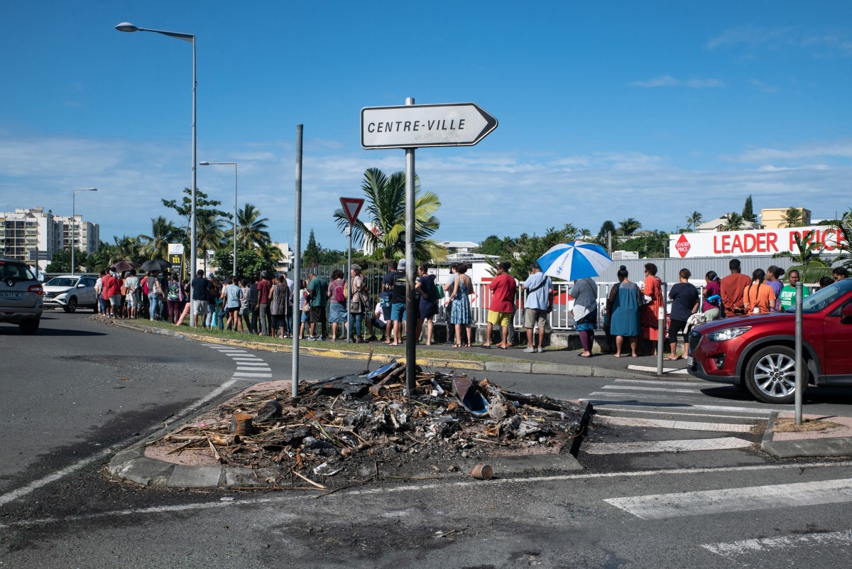 Des personnes font la queue pour acheter des provisions dans un supermarché alors que des articles carbonisés précédemment incendiés sont visibles à la suite des troubles de la nuit dans le quartier de Magenta à Nouméa, territoire français de Nouvelle-Calédonie dans le Pacifique, le 18 mai 2024. (Photo Delphine Mayeur AFP)