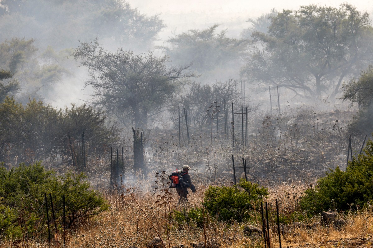 Un homme marche avec une soufflerie pour éteindre les incendies alors que des panaches de fumée s'élèvent d'un incendie dans un champ après que des roquettes lancées depuis le sud du Liban aient atterri près de Katzrin sur le plateau du Golan annexé par Israël, le 13 juin 2024, dans le cadre des affrontements transfrontaliers entre les troupes israéliennes et les combattants du Hezbollah. (Photo Jalaa MAREY / AFP)