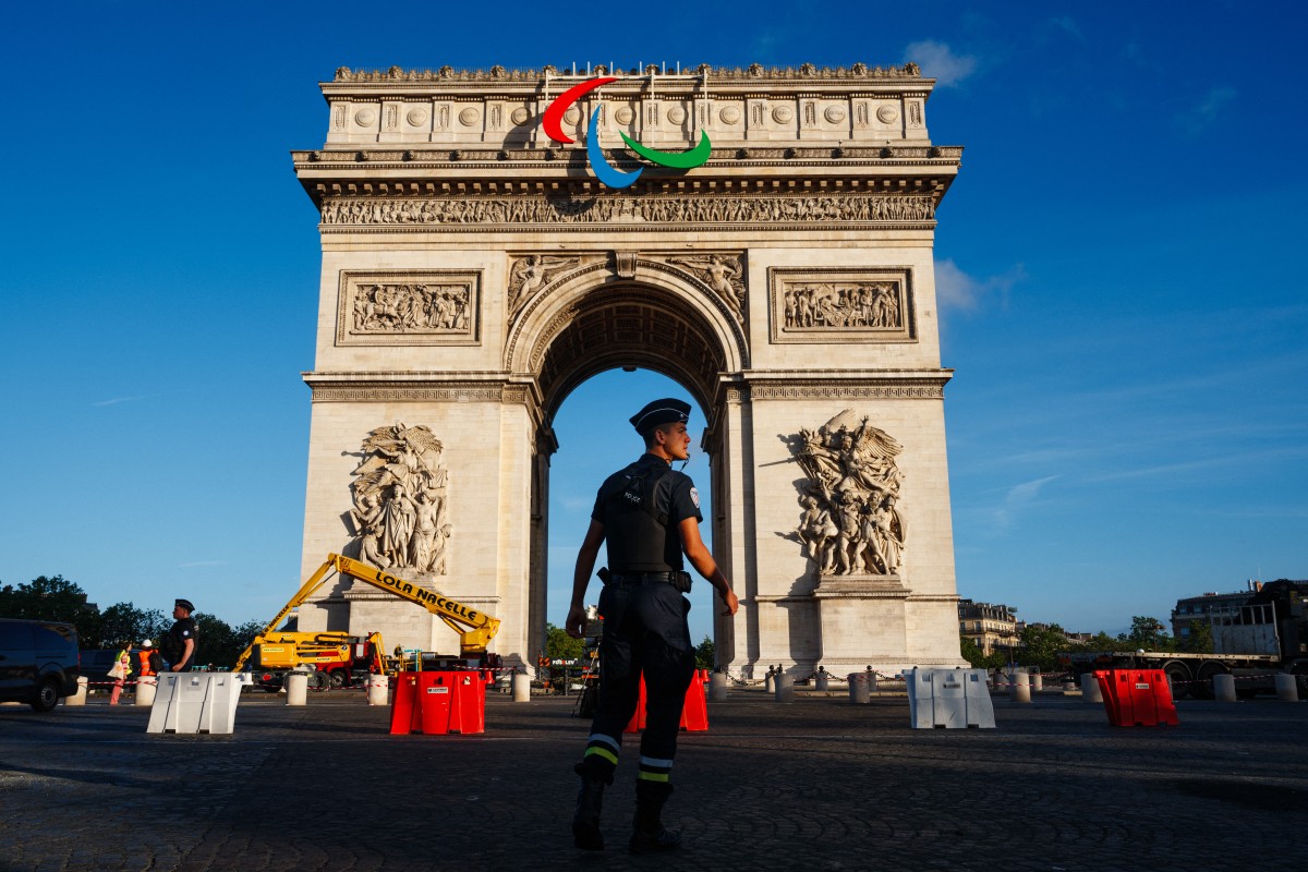 Un officier de police contrôle la circulation pendant que des ouvriers installent les Agitos, le symbole des Jeux Paralympiques sur l'Arc de Triomphe avant les prochains Jeux Olympiques et Paralympiques de Paris 2024, à Paris, le 28 juin 2024. (Photo par Dimitar DILKOFF / AFP)