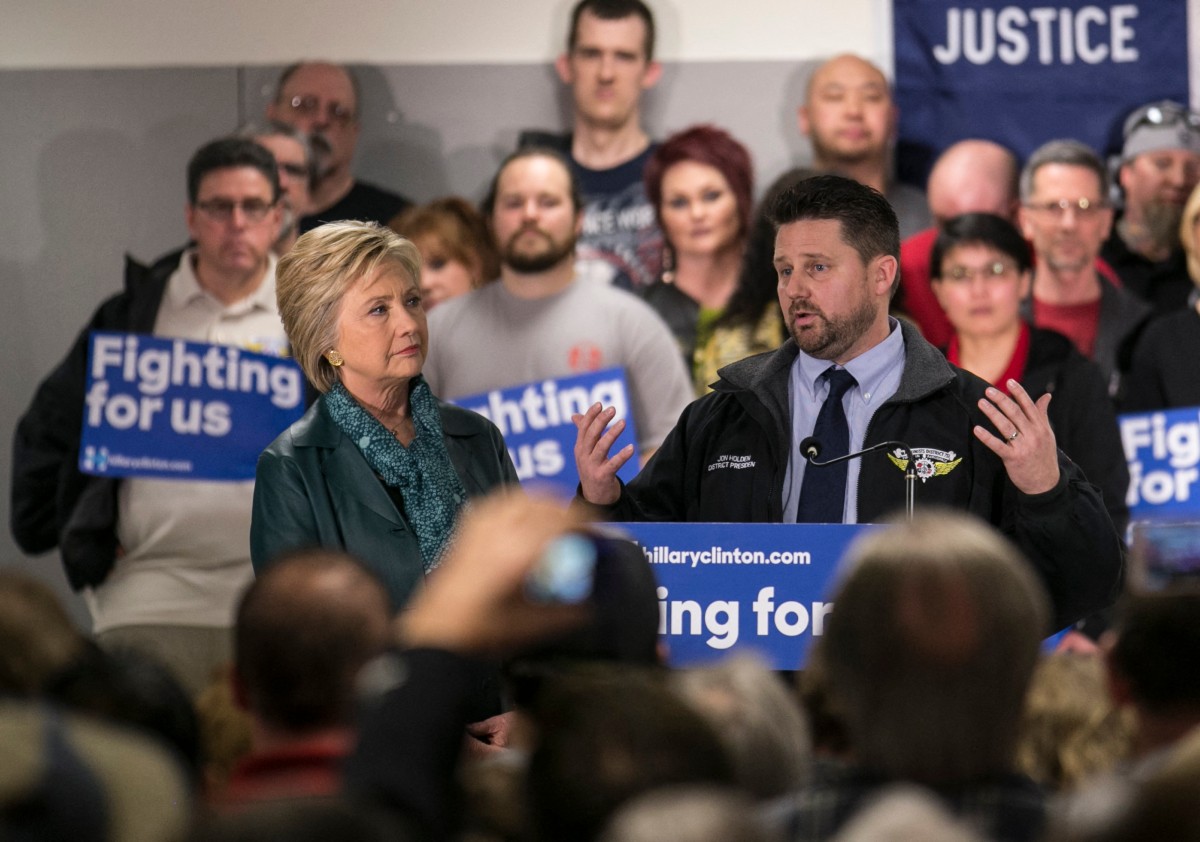 Le président du district 751 de l'Association internationale des machinistes et des travailleurs de l'aérospatiale, Jon Holden (à droite), s'exprime pendant que la candidate démocrate à la présidence, Hillary Clinton, l'écoute lors d'un rassemblement syndical le 22 mars 2016 à Everett, dans l'État de Washington. (Photo par STEPHEN BRASHEAR / GETTY IMAGES NORTH AMERICA / AFP)