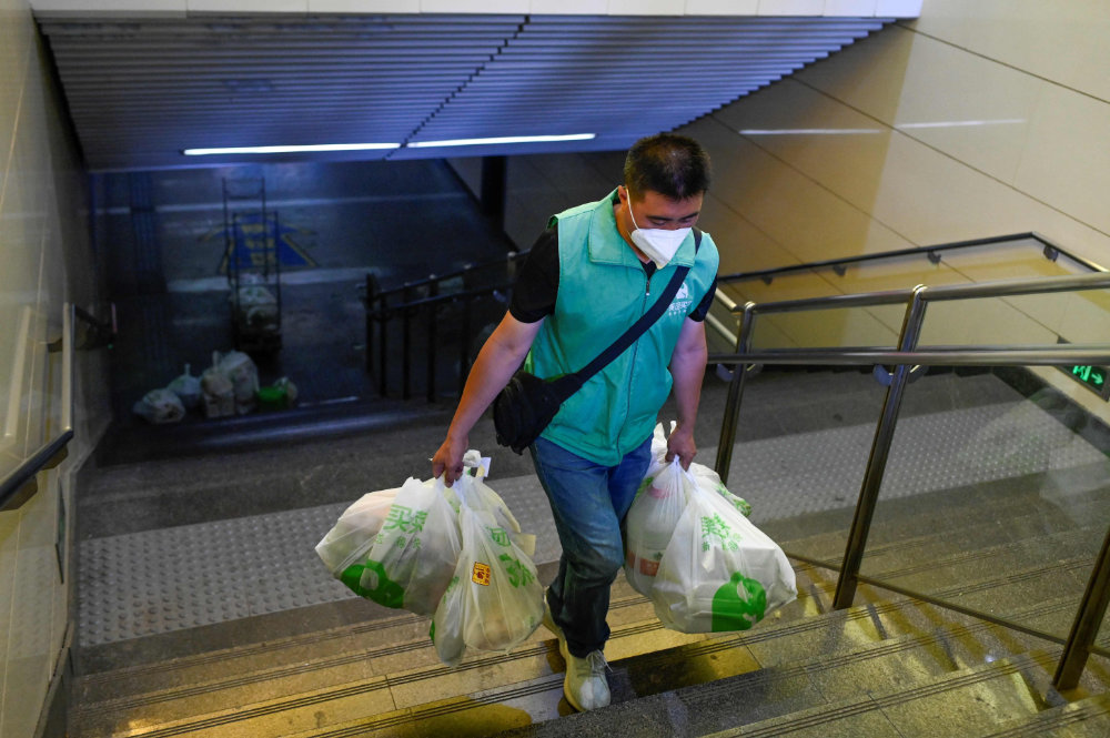 A delivery worker carries bags of food and water out of a subway station in Beijing. (AFP)