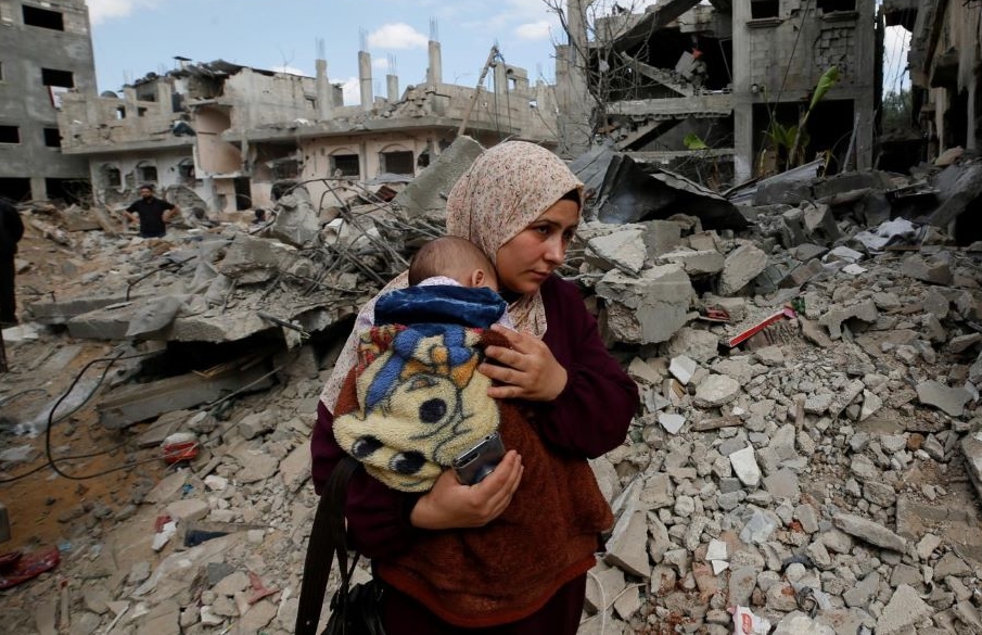 A Palestinian woman carries her child, amid rubble, after Israeli air strikes on the Gaza Strip, May 23, 2021. (Reuters)
