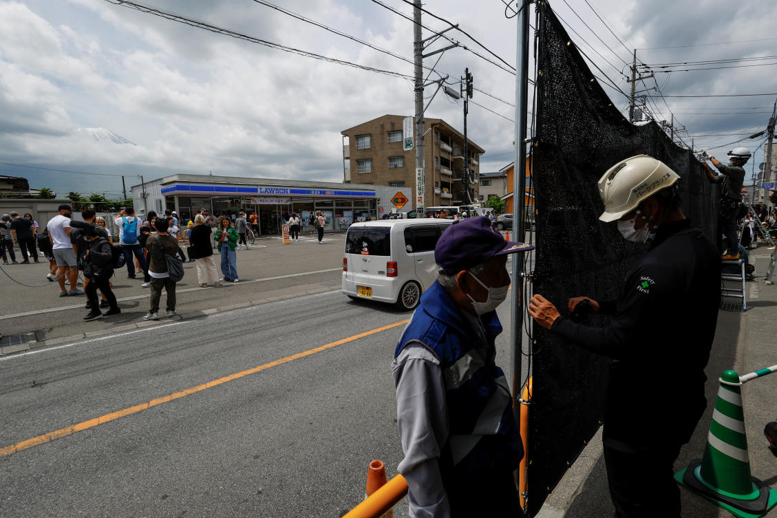 Tourists stand nearby as workers erect a barrier to block the view of a popular Mount Fuji photo spot, near a convenience store in Fujikawaguchiko town, Yamanashi prefecture, Japan on May 21, 2024. (Reuters)