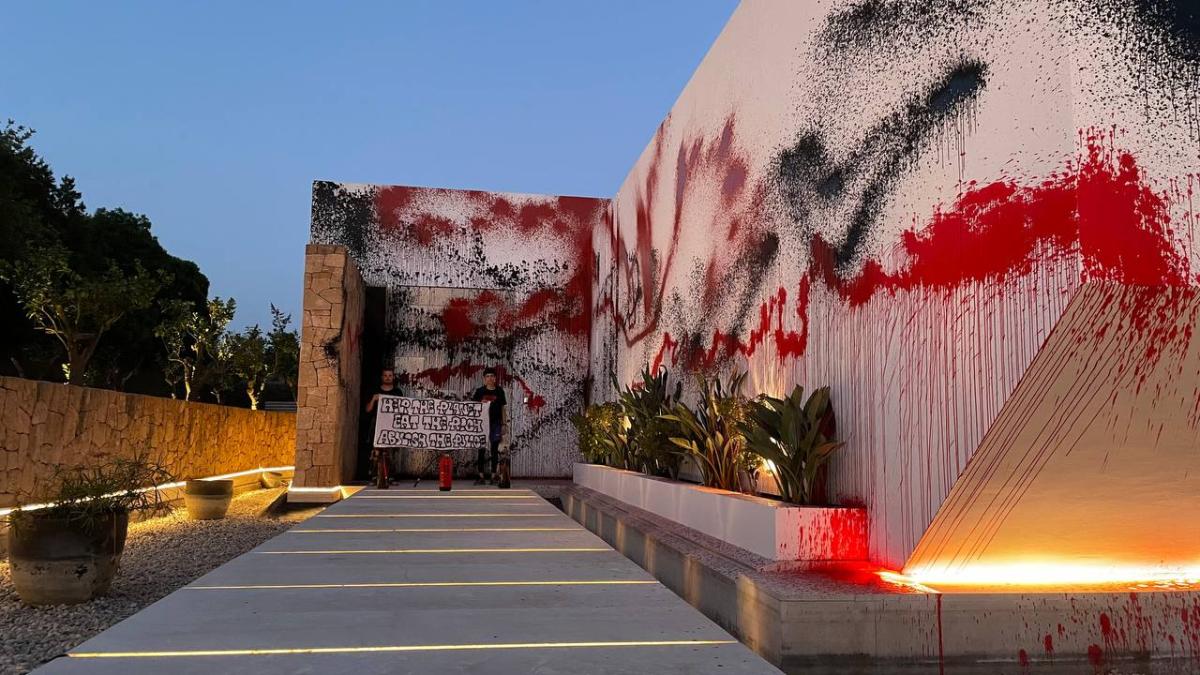 This handout photograph taken and released on August 6, 2024 by civil disobidience collective Futuro Vegetal shows two activists holding a banner reading "Help the planet, eat the rich, abolish the police" after spray-painting the house of Argentine football star Lionel Messi in Ibiza. (AFP)