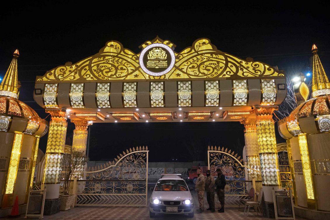 This picture taken on February 2, 2025 shows Afghan security guards standing at an entrance of a wedding hall, at night in Kabul. As night settles over Afghanistan's capital, only a few small lights and neon signs pierce the darkness and thick blanket of winter pollution. But on some street corners, glittering colossal wedding halls loom out of the gloom. (AFP)