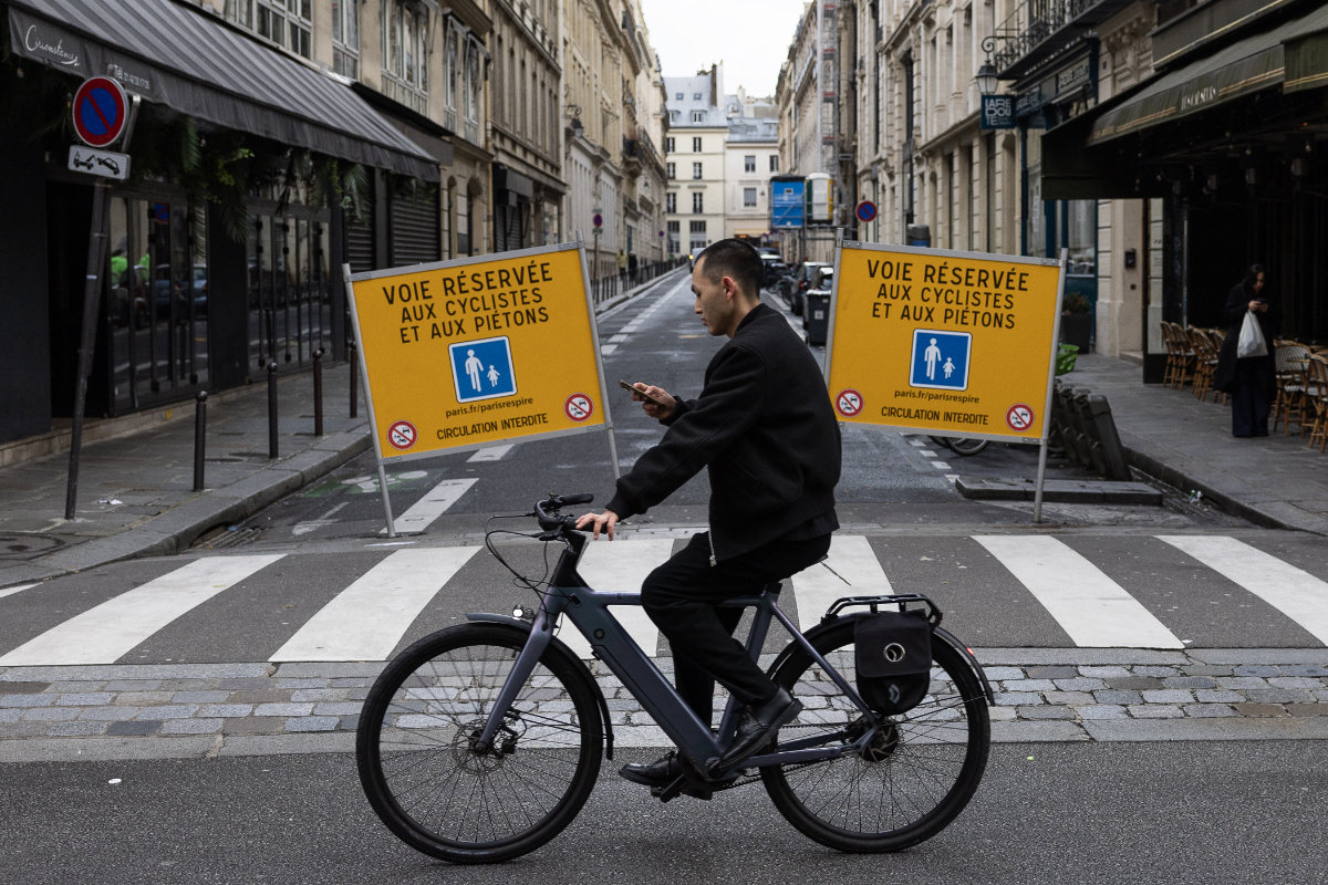 A man checks his mobile phone as he rides an electric bicycle past barriers, signaling the road reserved for pedestrians and cyclists, in Paris. (AFP)