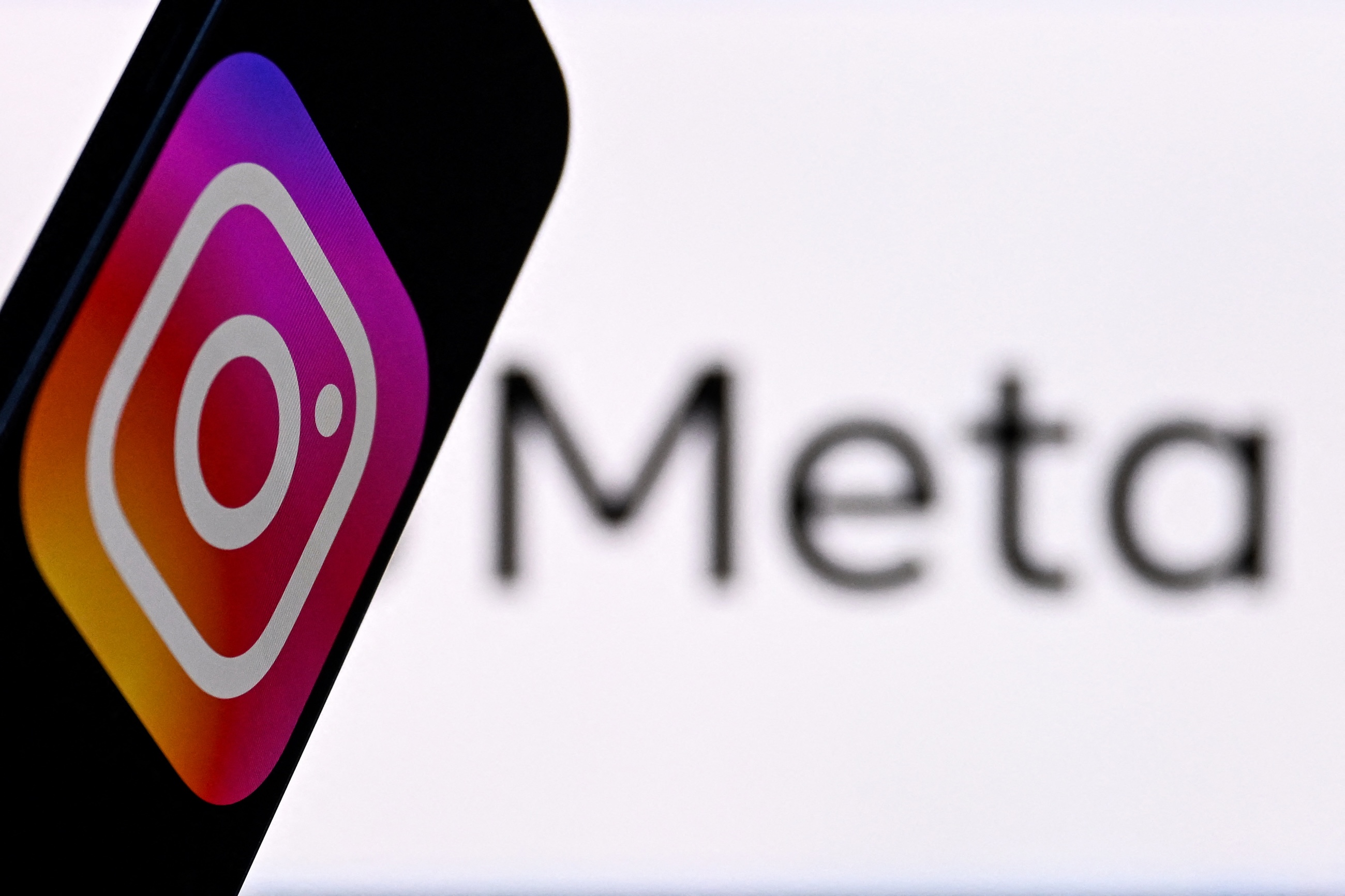 US social network Instagram logo displayed on a smartphone in front of the media giant Meta's logo on a laptop screen. (AFP)