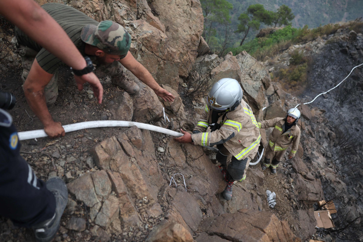 Firefighters climb a hill to contain a forest fire amid a heat wave in Latakia, Syria, on July 14, 2025. (AFP)