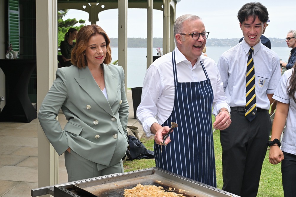 Australian Prime Minister Anthony Albanese reacts as he cooks on a barbecue with Minister for Communications Anika Wells, left, at an event to mark the beginning of the social media ban for children under 16 years of age, at Kirribilli House in Sydney, Australia, Wednesday, Dec. 10, 2025. (AAP Image/AP)