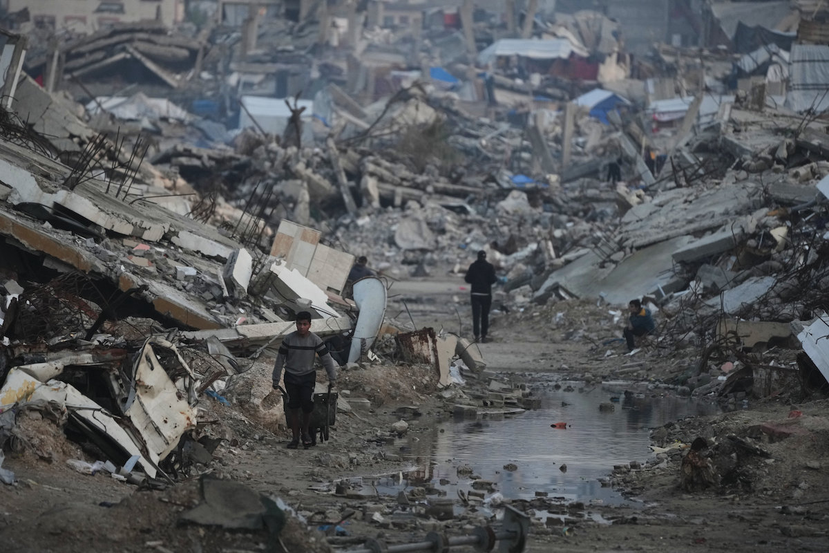 Palestinians walk amid buildings destroyed by Israeli air and ground operations in Gaza City. (AP)