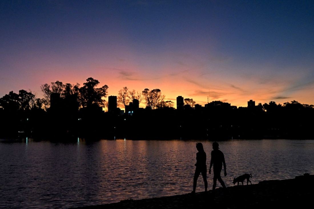 A couple walks with its dog around the Regatas lake at sunset in Buenos Aires, Argentina. (AFP)