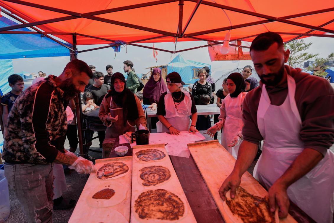 Soubhiye Zeiter, 63, center left, a displaced woman who fled her home with her family in Beirut’s southern suburbs, prepares with other workers mana’eesh to be distributed for displaced people at a small bakery in a tented settlement along Beirut’s waterfront, May 21, 2026. (AP)