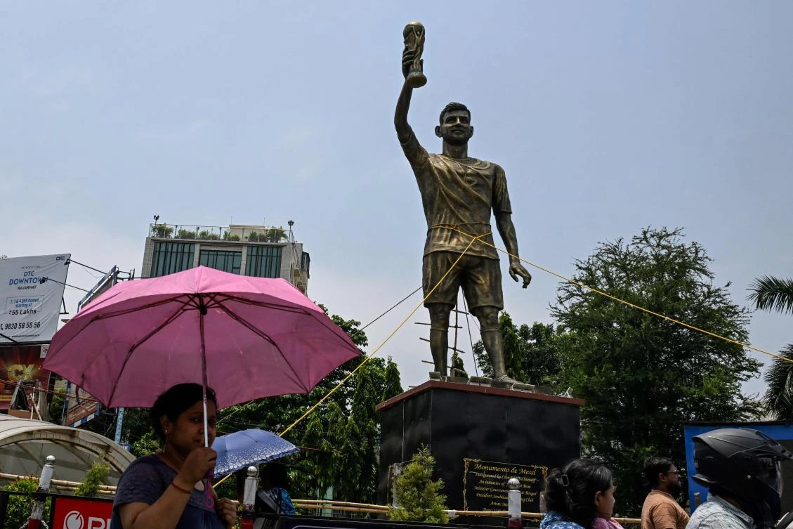 Commuters walk past a statue of Argentine football player Lionel Messi that has been tied with rope for stability from rain and thunderstorms In Kolkata on May 27, 2026. (AFP)