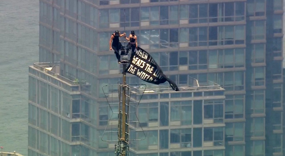 Two people stand on the tip of the antenna of the Empire State Building in New York while holding a banner on Wednesday, July 1, 2026. (WABC-TV/AP)