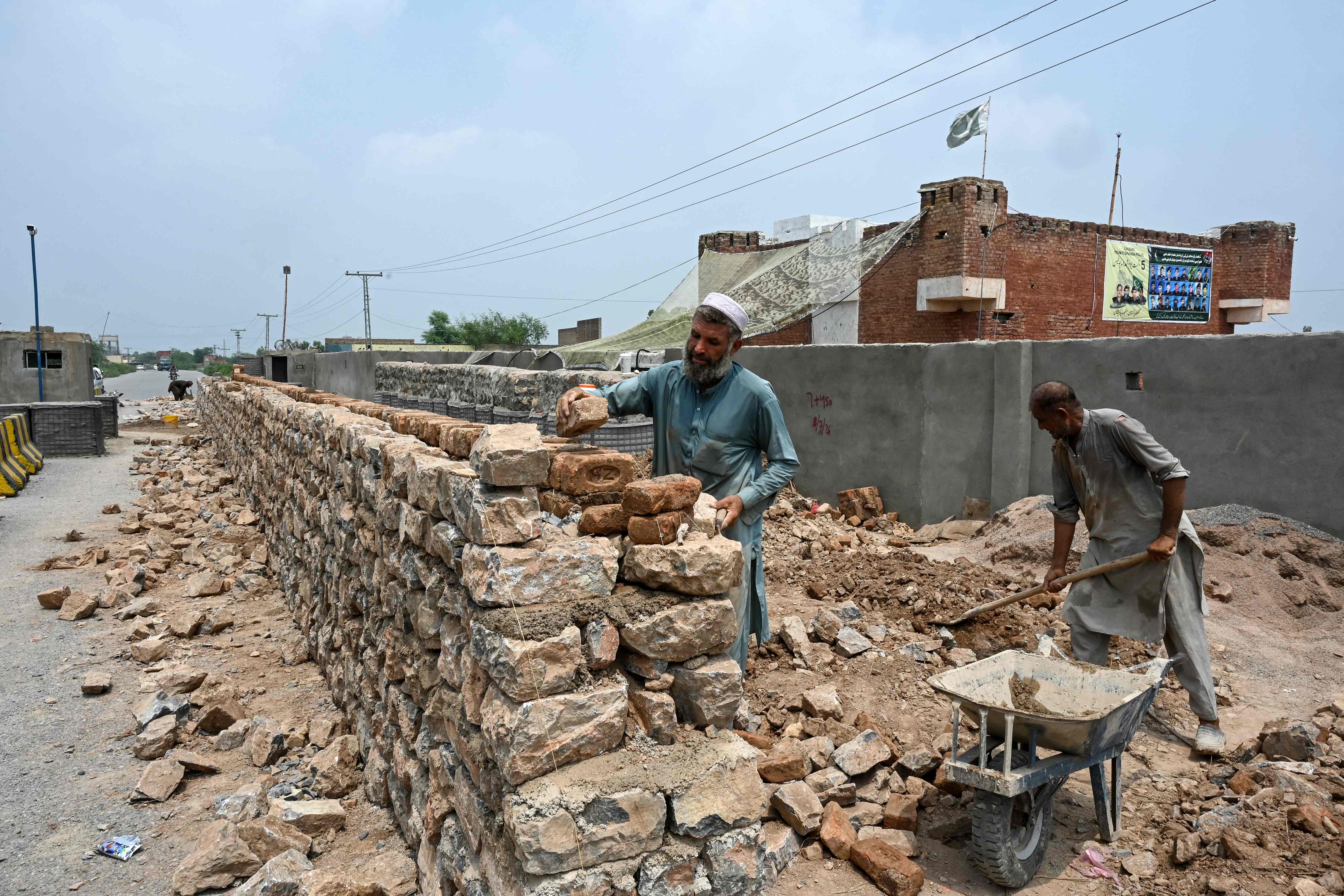 This photograph, taken on August 4, 2026, shows workers constructing a boundary wall around a police post fortified with Ukraine-style mesh barriers, serving as a new line of defense against militant drone and aerial attacks in Bara, Khyber Pakhtunkhwa province, Pakistan. (AFP)